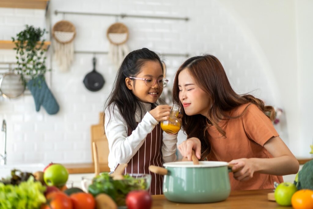 Menina em uma cozinha direcionando um pote com substância amarela dentro para uma mulher sentir o cheiro 