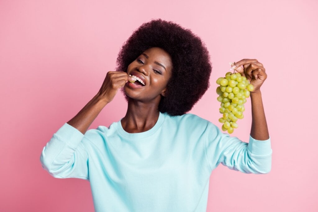 mulher de blusa azul segurando e comendo uva verde