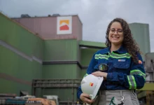 Mulher branca de cabelos cacheados, uniformizada, segurando um capacete branco com a marca Ternium
