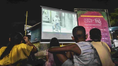 Crianças sentadas na rua assistindo um filme em uma projeção na parede