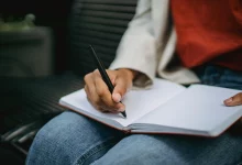 Pessoa preta sentada, com um caderno apoiado nas pernas, enquanto escreve