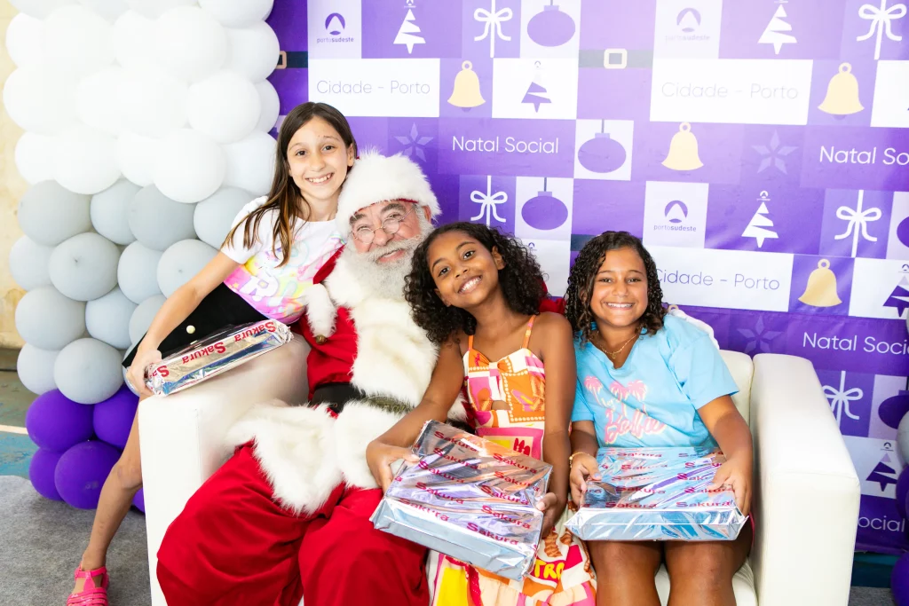 Três crianças com presentes nas mãos, sorrindo ao lado de Papai Noel