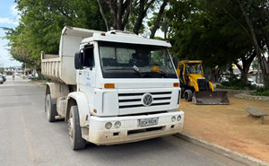 primeiro plano aparece um caminhão truck e ao fundo uma retroescavadeira estacionados