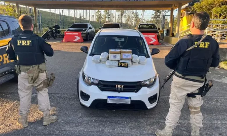 Policiais rodoviários federais ao lado da viatura exibem os 21 quilos de drogas apreendidos
