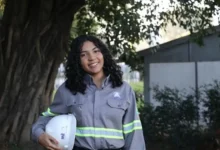 Estagiária uniformizada sorrindo com capacete embaixo do braço